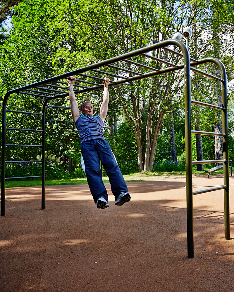 A man hangs from horizontal ladder at an outdoor fitness gym.